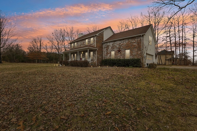 back of property at dusk featuring a garage, brick siding, a yard, and a chimney