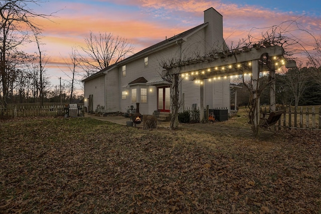 back of house at dusk with entry steps, central AC unit, fence, and a chimney