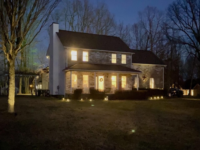 back of house at twilight featuring stone siding and a chimney