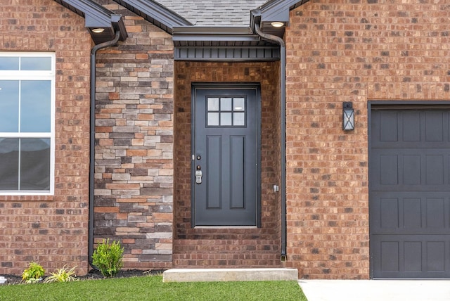 view of exterior entry with brick siding, an attached garage, and roof with shingles