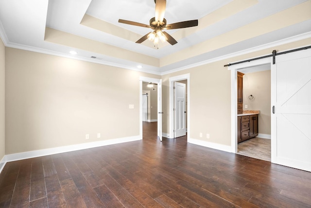 unfurnished bedroom featuring baseboards, a raised ceiling, a barn door, and wood-type flooring