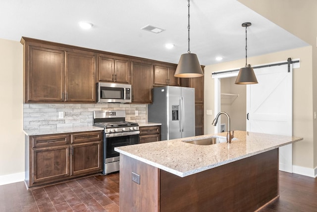 kitchen featuring visible vents, a sink, stainless steel appliances, a barn door, and tasteful backsplash