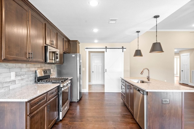 kitchen featuring visible vents, a barn door, decorative backsplash, stainless steel appliances, and a sink