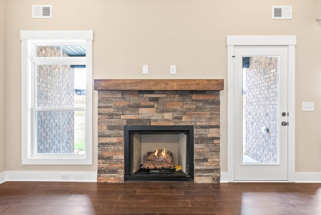 interior details with a stone fireplace, wood finished floors, visible vents, and baseboards