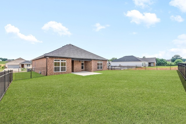 rear view of house with brick siding, a shingled roof, a lawn, a fenced backyard, and a patio area