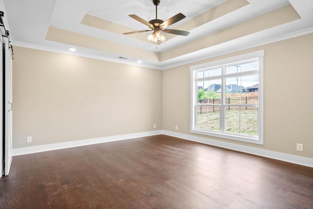 empty room with a ceiling fan, a barn door, dark wood-style floors, and a raised ceiling