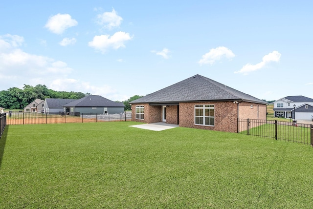 rear view of house featuring a lawn, a patio, a fenced backyard, a shingled roof, and brick siding