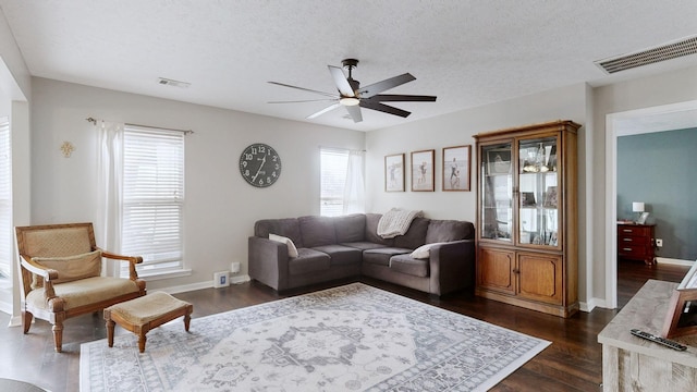 living room featuring visible vents, a textured ceiling, dark wood-type flooring, and a ceiling fan