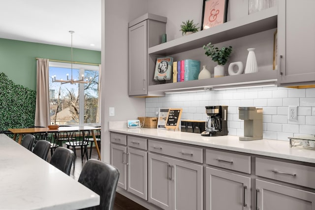 kitchen with tasteful backsplash, gray cabinetry, light stone counters, a notable chandelier, and open shelves