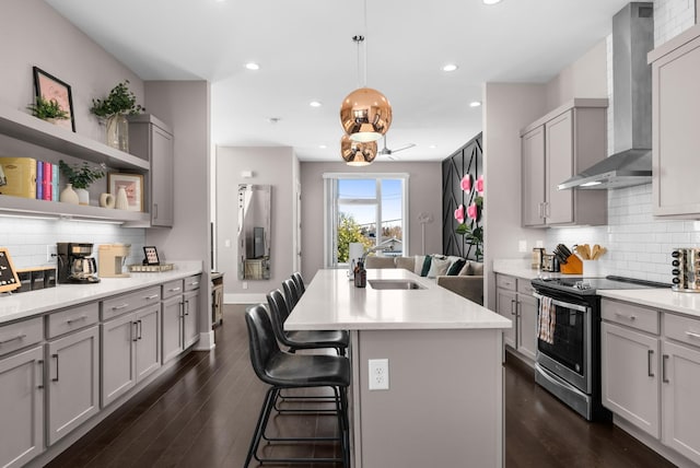 kitchen featuring stainless steel range with electric stovetop, wall chimney exhaust hood, gray cabinetry, and a sink