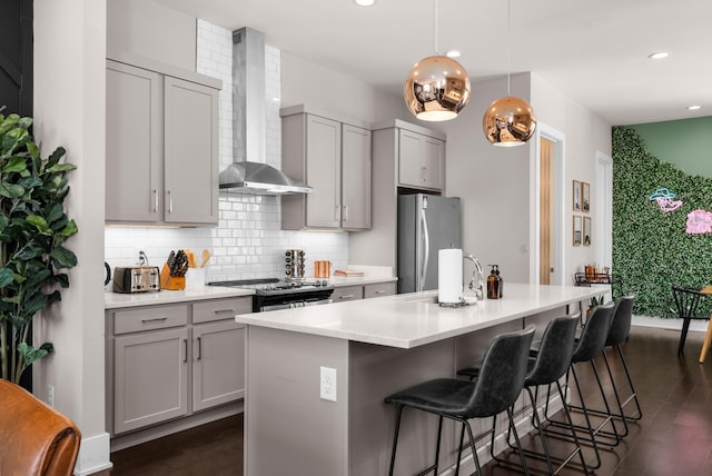 kitchen with backsplash, gray cabinets, appliances with stainless steel finishes, a kitchen breakfast bar, and wall chimney exhaust hood