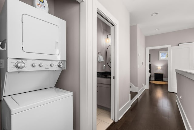 laundry area with wood finished floors, baseboards, stacked washing maching and dryer, laundry area, and recessed lighting