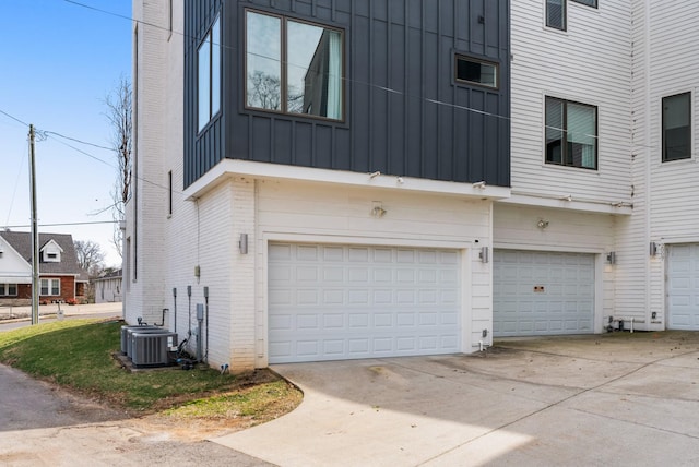 view of side of property featuring central AC unit, concrete driveway, a garage, board and batten siding, and brick siding