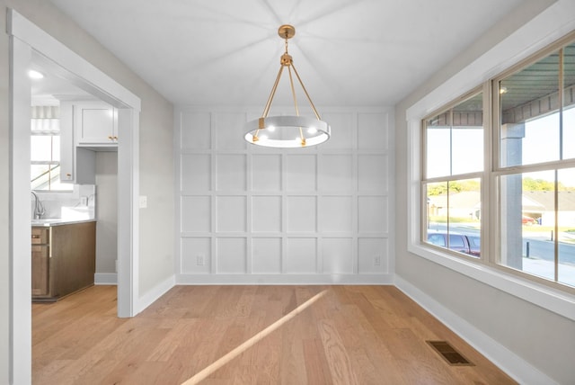 unfurnished dining area featuring visible vents, baseboards, a decorative wall, and light wood-style floors