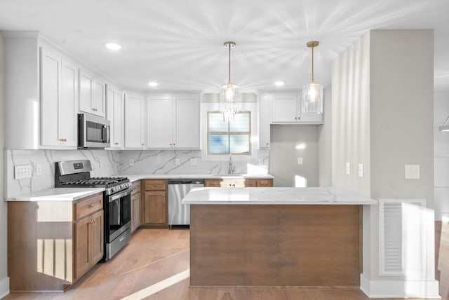 kitchen with visible vents, a peninsula, stainless steel appliances, decorative backsplash, and pendant lighting