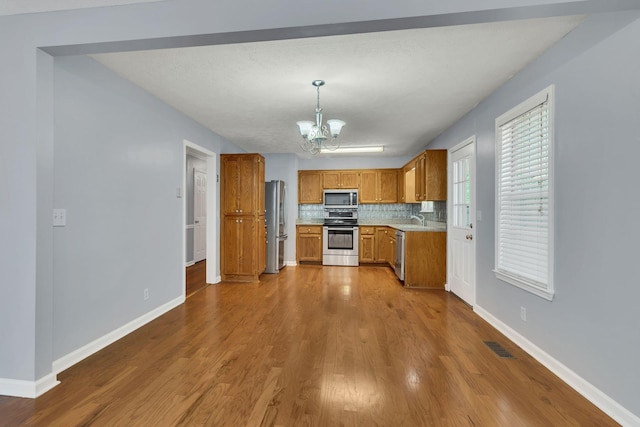 kitchen featuring brown cabinetry, a sink, decorative backsplash, stainless steel appliances, and a notable chandelier