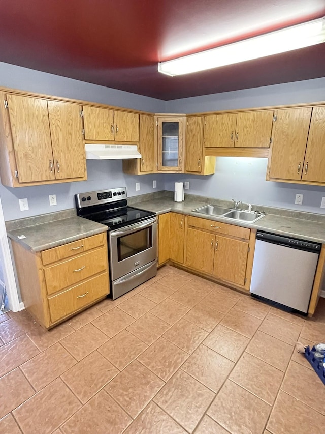 kitchen with under cabinet range hood, a sink, appliances with stainless steel finishes, light tile patterned floors, and glass insert cabinets