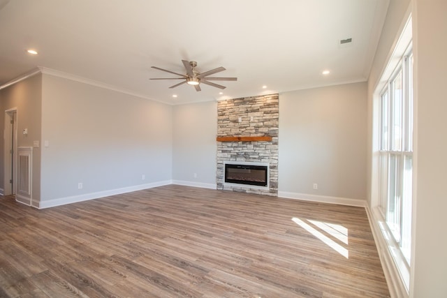 unfurnished living room with baseboards, ornamental molding, a stone fireplace, wood finished floors, and a ceiling fan