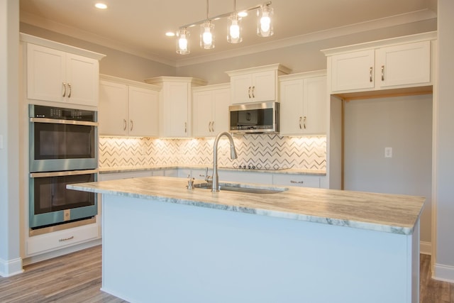 kitchen featuring an island with sink, ornamental molding, a sink, white cabinetry, and appliances with stainless steel finishes