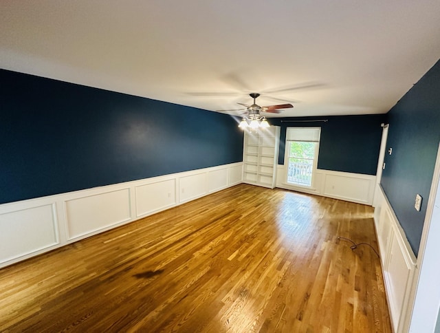 unfurnished room featuring wood finished floors, wainscoting, and ceiling fan