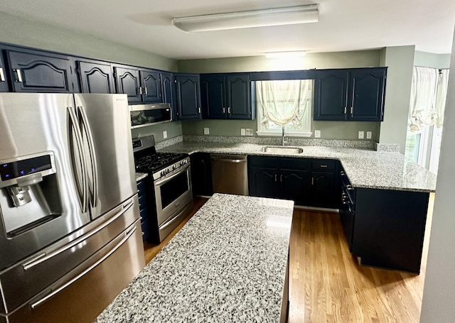 kitchen with light stone countertops, a peninsula, a sink, appliances with stainless steel finishes, and light wood-type flooring