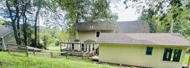 rear view of property featuring a yard, fence, roof with shingles, and a wooden deck