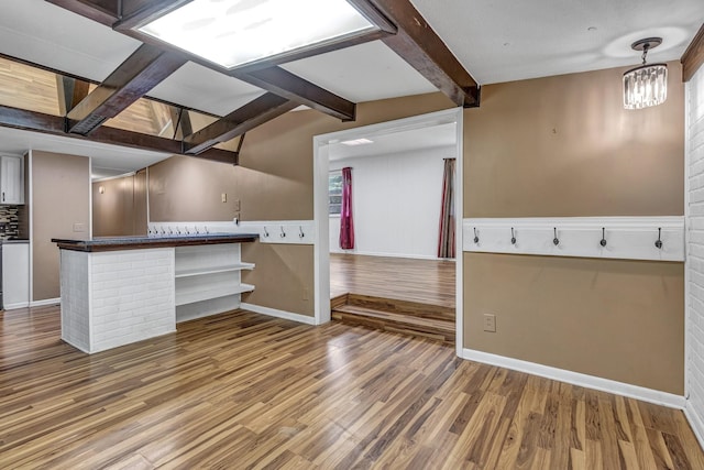 interior space featuring wood finished floors, baseboards, vaulted ceiling with beams, dark countertops, and a notable chandelier