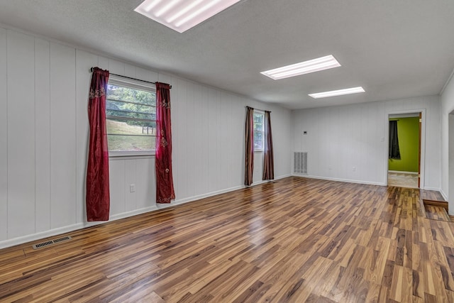 empty room featuring visible vents, baseboards, a textured ceiling, and wood finished floors