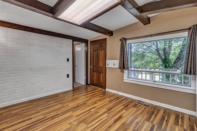 empty room with baseboards, visible vents, brick wall, lofted ceiling with beams, and light wood-type flooring