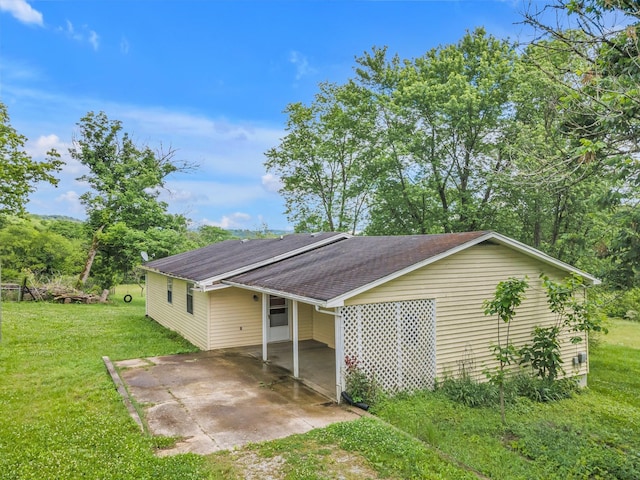 exterior space featuring an attached carport, roof with shingles, a lawn, driveway, and a patio