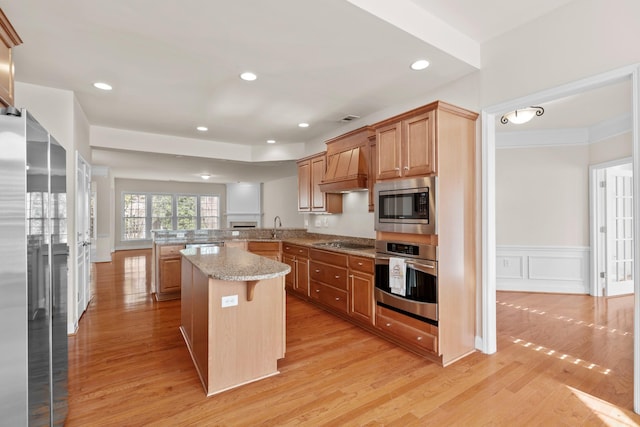 kitchen with light wood-type flooring, a peninsula, custom exhaust hood, stainless steel appliances, and a sink