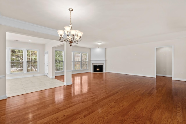 unfurnished living room with a chandelier, a warm lit fireplace, baseboards, and wood finished floors