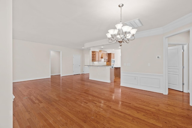 unfurnished living room with a wainscoted wall, visible vents, light wood finished floors, crown molding, and a notable chandelier