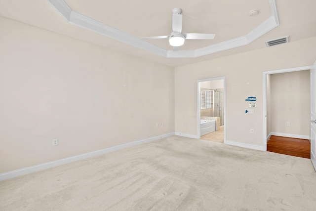 unfurnished bedroom featuring visible vents, light carpet, ornamental molding, a tray ceiling, and baseboards