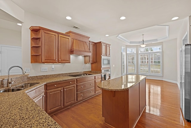 kitchen featuring a raised ceiling, light wood-style floors, stainless steel appliances, and a sink