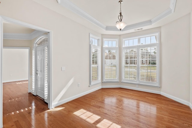 interior space with visible vents, a raised ceiling, wood finished floors, and ornamental molding