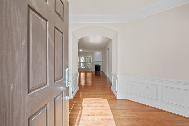 interior space with a wainscoted wall, light wood-style flooring, arched walkways, a fireplace, and a decorative wall