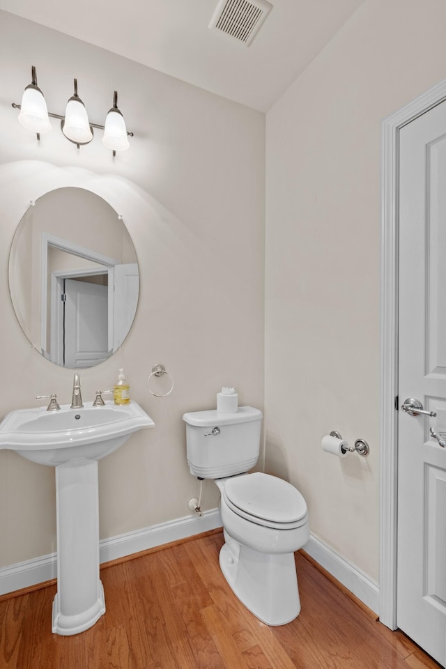 bathroom with visible vents, baseboards, toilet, wood finished floors, and a sink