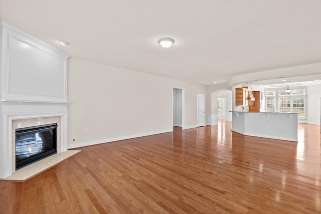 unfurnished living room featuring baseboards, light wood-style floors, arched walkways, and a premium fireplace