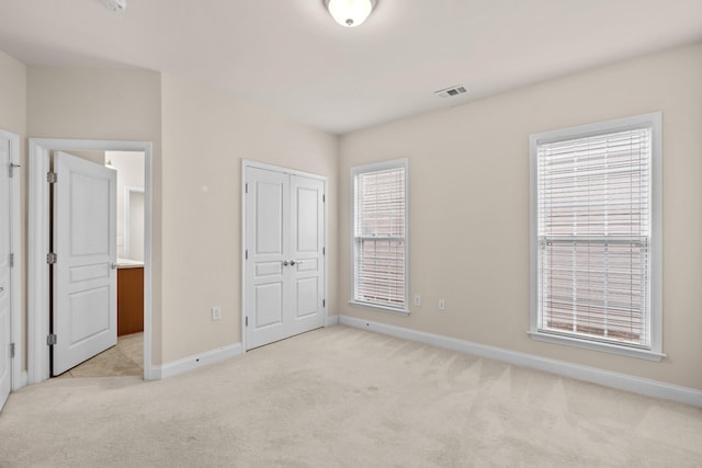 unfurnished bedroom with light colored carpet, visible vents, a closet, and baseboards