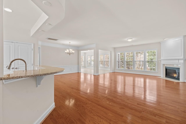 unfurnished living room with visible vents, a fireplace with flush hearth, wood finished floors, an inviting chandelier, and a decorative wall