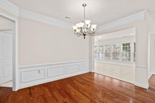 unfurnished dining area featuring an inviting chandelier, crown molding, wood finished floors, and visible vents