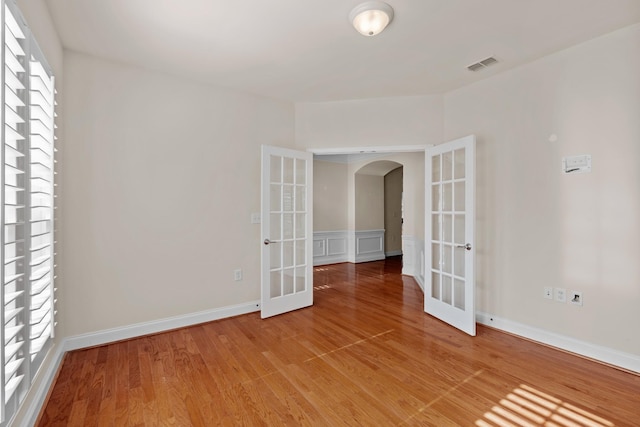 empty room with arched walkways, visible vents, light wood-style flooring, and french doors