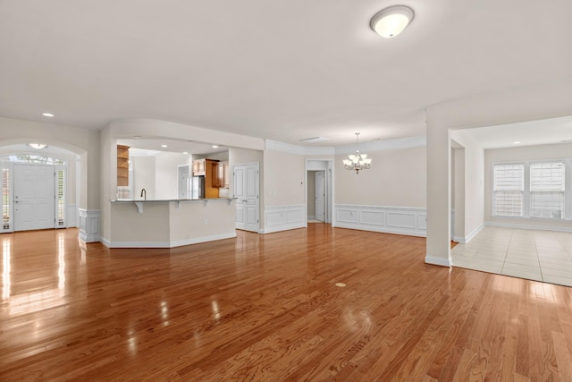 unfurnished living room with an inviting chandelier, a decorative wall, light wood-style floors, and a wainscoted wall