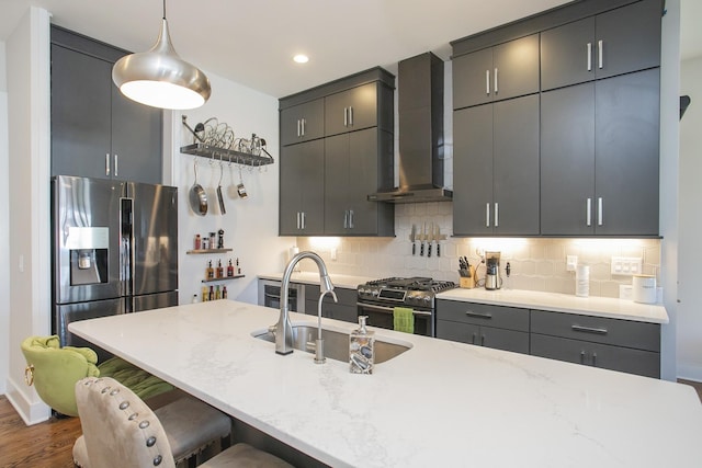 kitchen featuring wall chimney range hood, a breakfast bar area, decorative backsplash, appliances with stainless steel finishes, and a sink