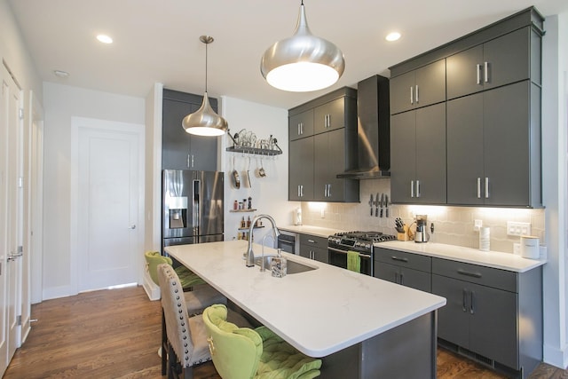 kitchen featuring wall chimney range hood, a sink, appliances with stainless steel finishes, a kitchen breakfast bar, and backsplash