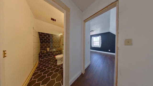 hall featuring baseboards, lofted ceiling, and wood finished floors