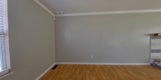 empty room with crown molding, wood finished floors, baseboards, and visible vents