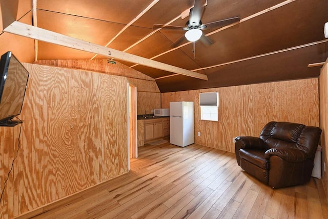 living area featuring lofted ceiling, light wood-style flooring, a ceiling fan, and wood walls