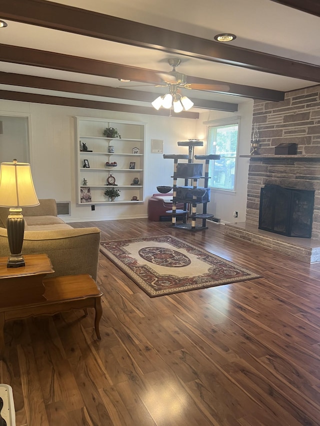 living room with built in features, wood finished floors, a ceiling fan, beam ceiling, and a fireplace